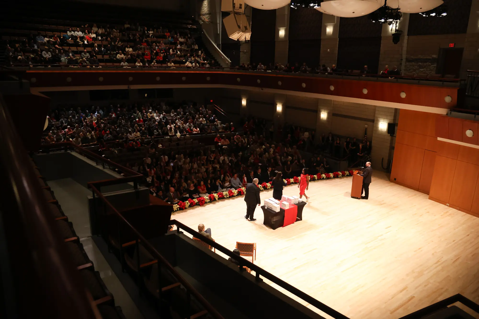 A wide angle shot depicting Hugh Hodgson Concert Hall during Grady College's 2025 Convocation, with three figures on stage in front of a crowd of people.
